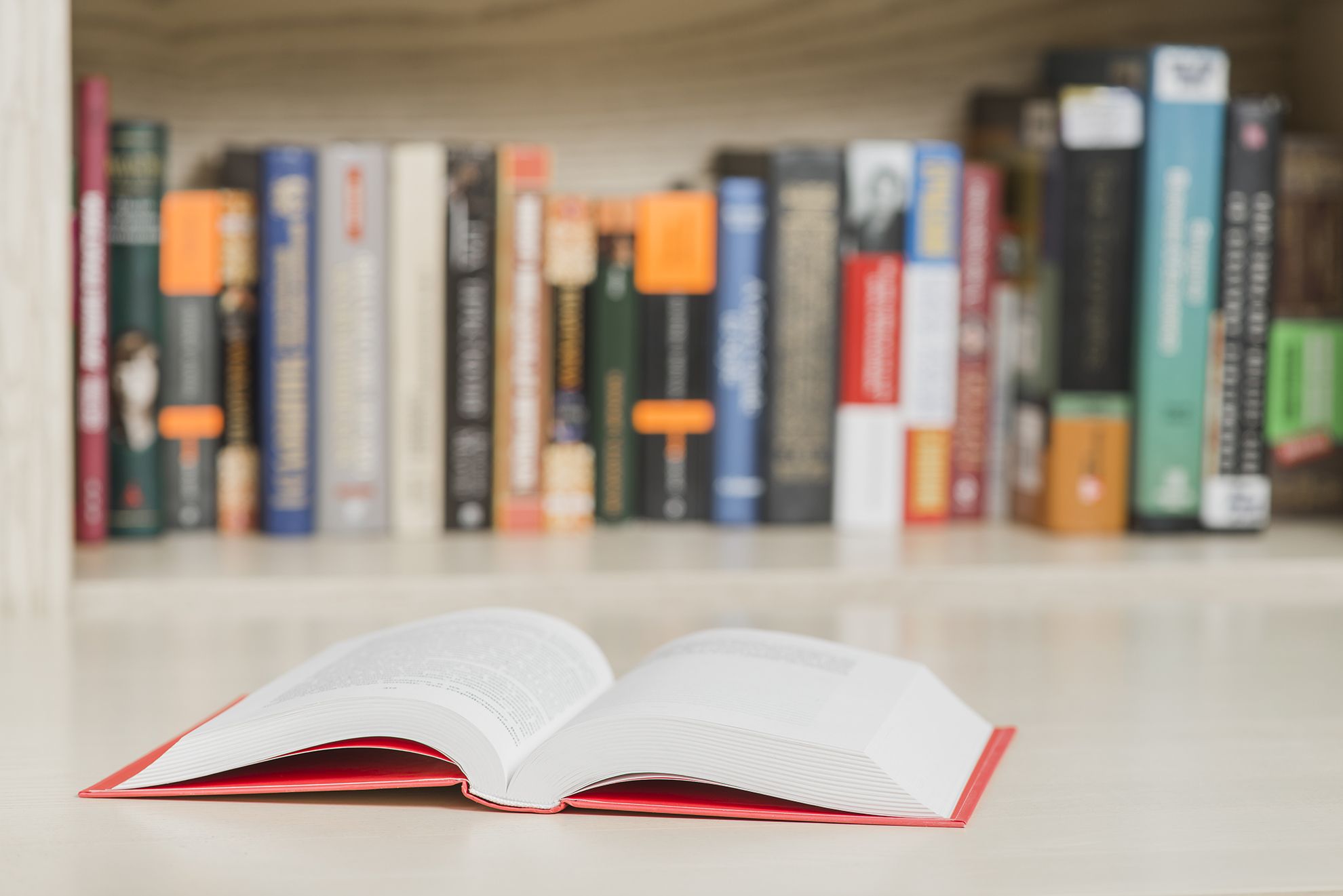 Livre relié ouvert avec reliure rouge exposé devant d'autres livres imprimés sur une étagère. Cette image montre la finition professionnelle et la qualité de reliure obtenues grâce aux services d'impression professionnelle de livres. Représentation parfaite d'un livre imprimé de haute qualité et prêt pour la distribution.
