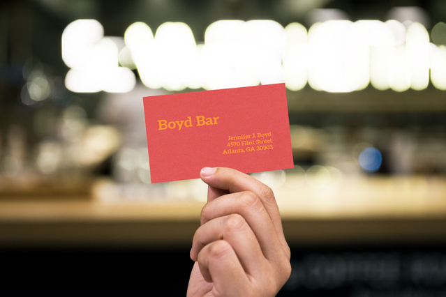 Carte de visite rouge Boyd Bar en papier coloré tenue devant un bar Carte Boyd Bar rouge sur papier Sirio Fedrigoni avec texte jaune. Cartes couleur 6 teintes dorure Sprint24.