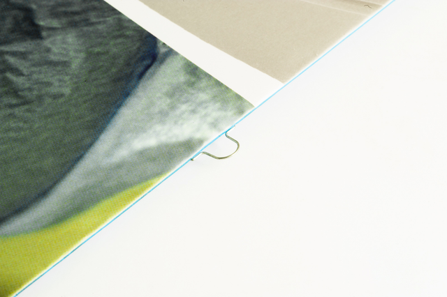 Vue rapprochée d'une reliure point Omega, montrant la piqûre métallique distinctive qui maintient les pages du livre. Idéale pour les brochures professionnelles, catalogues et documents reliés nécessitant une durabilité et une finition soignée. Parfait pour les projets d'impression personnalisés recherchant des solutions de reliure fiables.