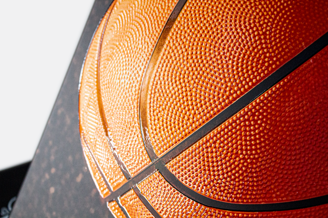 Gros plan macro d'une surface de ballon de basket montrant la texture orange granulée distinctive et les coutures noires, mettant en valeur les détails tactiles de surface. Les techniques de finition d'impression premium — vernis UV en relief, pelliculage soft-touch — créent des expériences tactiles similaires sur cartes de visite et matériaux imprimés.