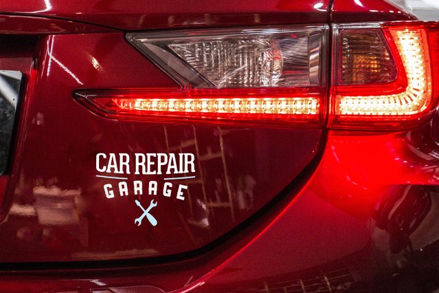 Lettrage adhésif blanc 'Car Repair Garage' appliqué à l'arrière d'une voiture rouge près du feu arrière. Sprint24 imprime des lettrages adhésifs personnalisés sur vinyle blanc brillant avec une durée de vie jusqu'à 60 mois — idéaux pour marquage véhicule, vitrines et signalétique avec application à sec sans bulles.
