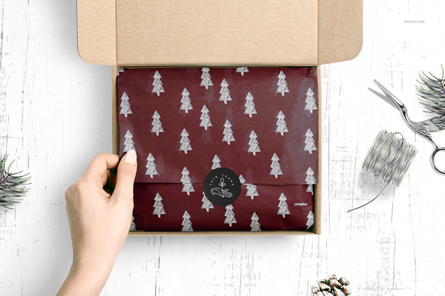 Main ouvrant boite kraft papier bordeaux motif sapins argent et sceau cire brande. Sprint24.