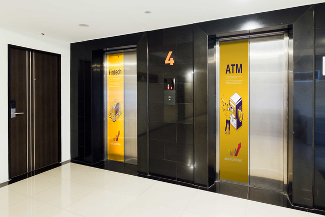 PVC adhésif grand format appliqué sur surfaces planes noires avec graphiques jaunes de signalétique comprenant distributeur ATM, numéros d'étage et icônes directionnelles pour espaces commerciaux modernes. Démontre installation professionnelle avec bords nets, application sans bulles et excellente durabilité dans environnements intérieurs à forte circulation. Parfait pour immeubles de bureaux, in…